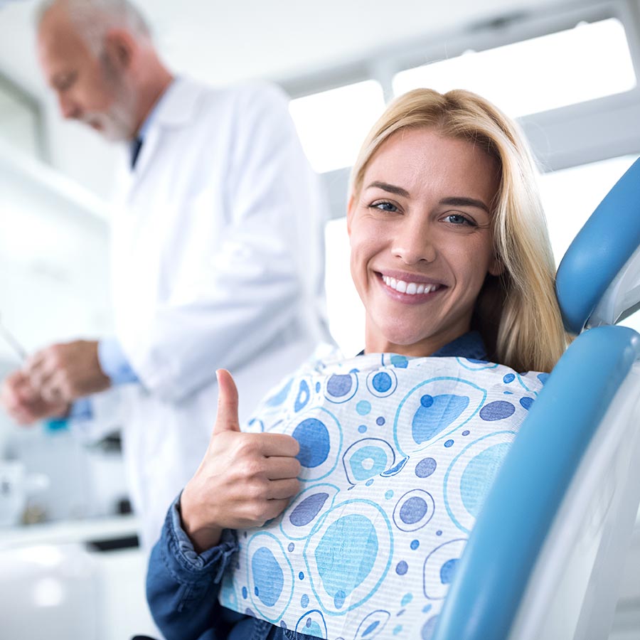 Mujer en clínica dental sonriendo y con el pulgar hacia arriba